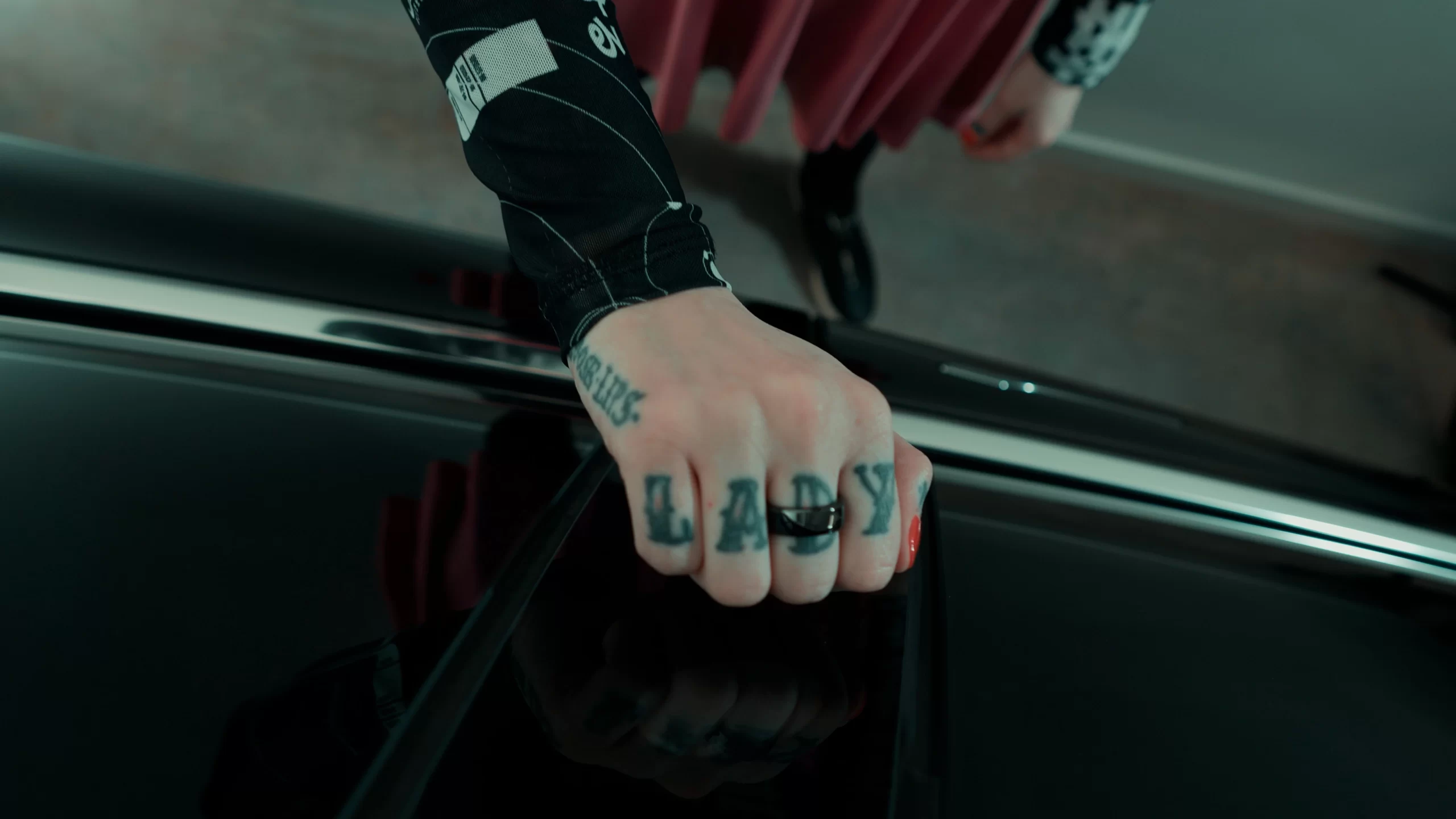 woman with tattoed hands wearing the Apex Ring and resting it over the hood of a black tesla