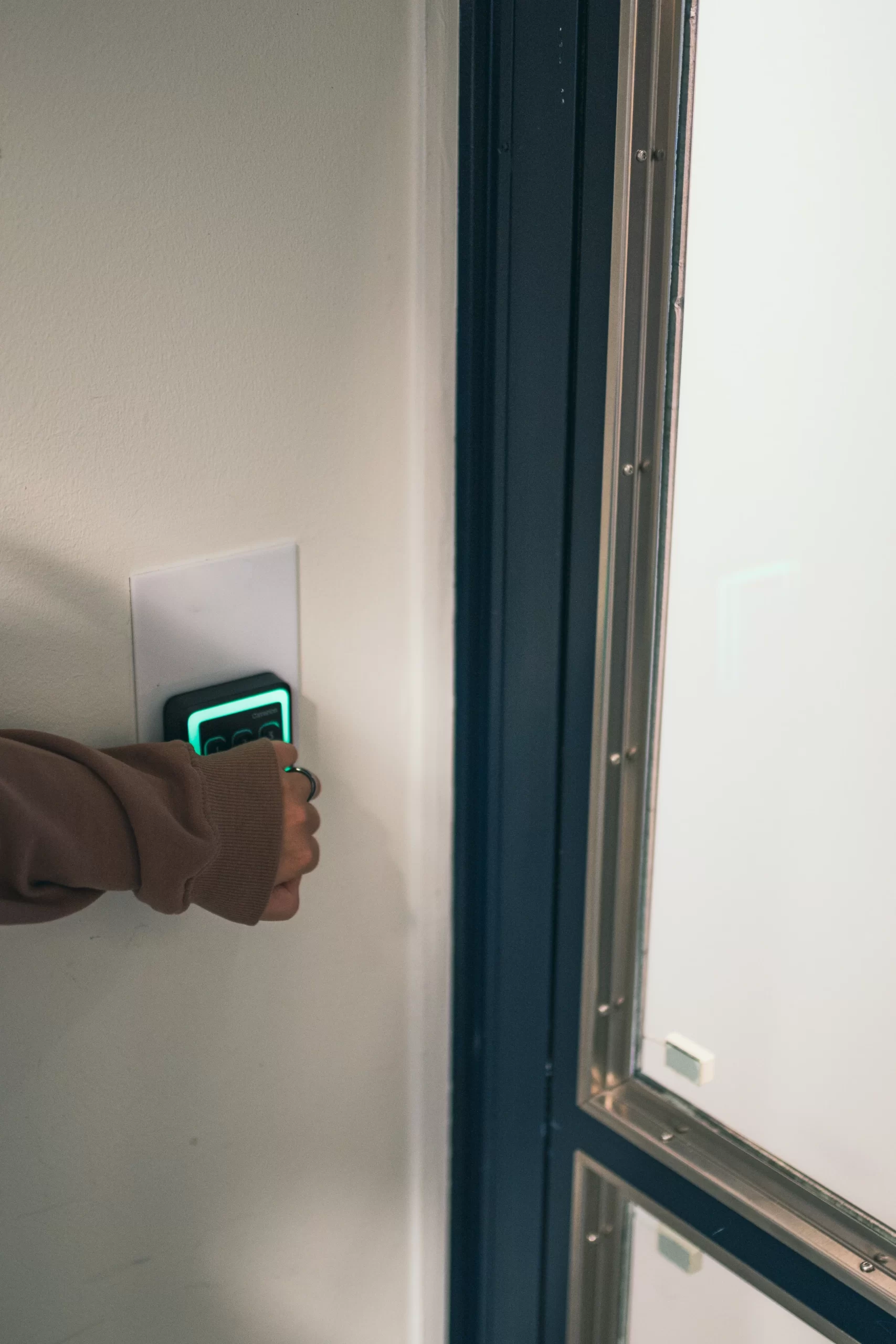 A woman's hand knocking on the access panel on the wall with a green light indicating access is granted
